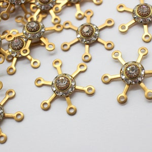 May include: A group of gold-toned metal snowflake charms with clear rhinestone accents. Each charm has six points and a central rhinestone.