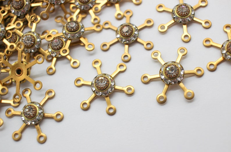 May include: A group of gold-toned metal snowflake charms with clear rhinestone accents. Each charm has six points and a central rhinestone.