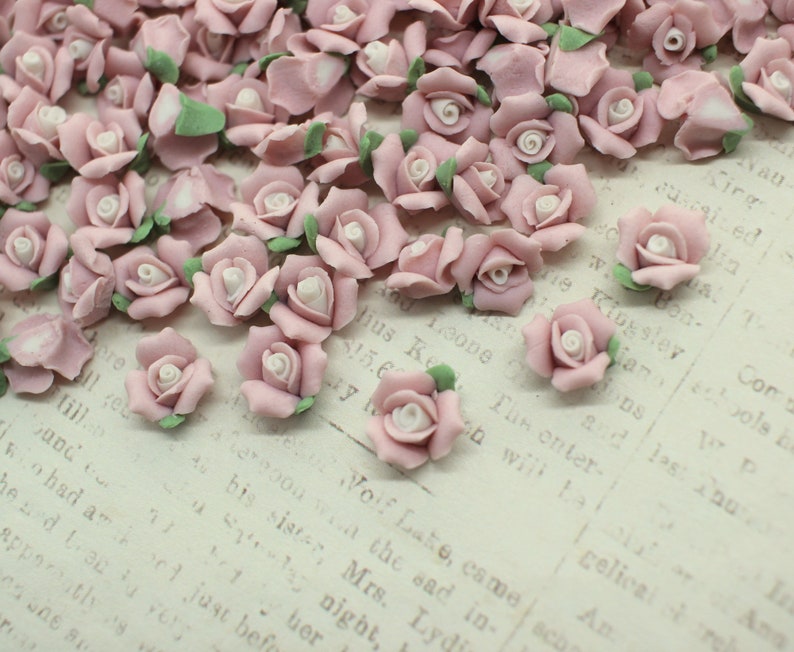 May include: A collection of small, delicate, pink rose blossoms with white centers and green leaves. The miniature roses are scattered across a textured, off-white surface, creating a soft, romantic aesthetic.