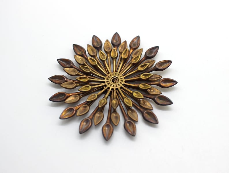 May include: A gold and brown metal sunburst wall decor with a circular center and radiating spokes with leaf-shaped ends.