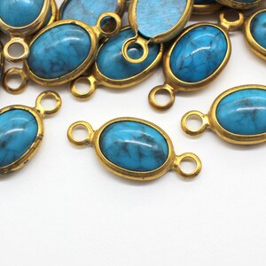 May include: A group of turquoise blue oval-shaped gemstone charms with gold-toned metal settings and two jump rings. The charms are scattered on a white surface.
