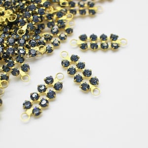 May include: A collection of gold-toned metal jewelry connectors featuring two parallel rows of small, round, dark blue faceted crystals. Each rectangular connector has a small circular loop at both ends for attachment to other jewelry components.