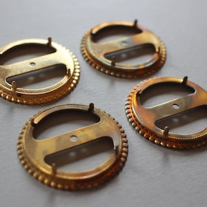 May include: Four gold-toned metal circular frames with a decorative beaded edge. Each frame has a center bar with two holes on either side.