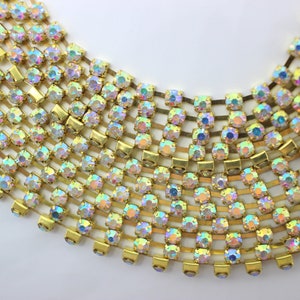 May include: A gold chain with iridescent rhinestones. The chain is made of small, square-shaped rhinestones that are connected by gold metal links. The rhinestones are arranged in a repeating pattern.