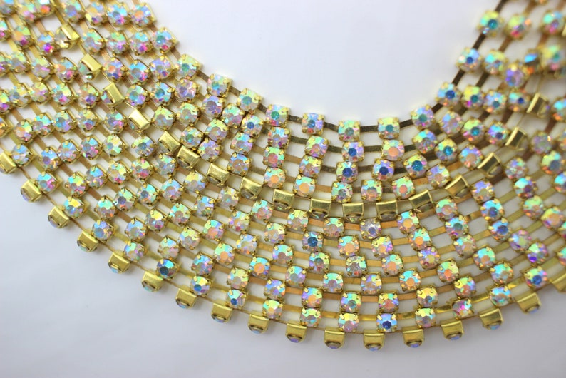 May include: A gold chain with iridescent rhinestones. The chain is made of small, square-shaped rhinestones that are connected by gold metal links. The rhinestones are arranged in a repeating pattern.