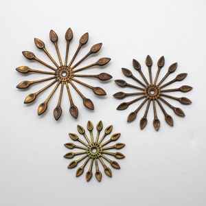 May include: Three gold-toned metal decorative pieces in the shape of a sunburst with pointed rays. The pieces are different sizes and have a slightly aged finish.