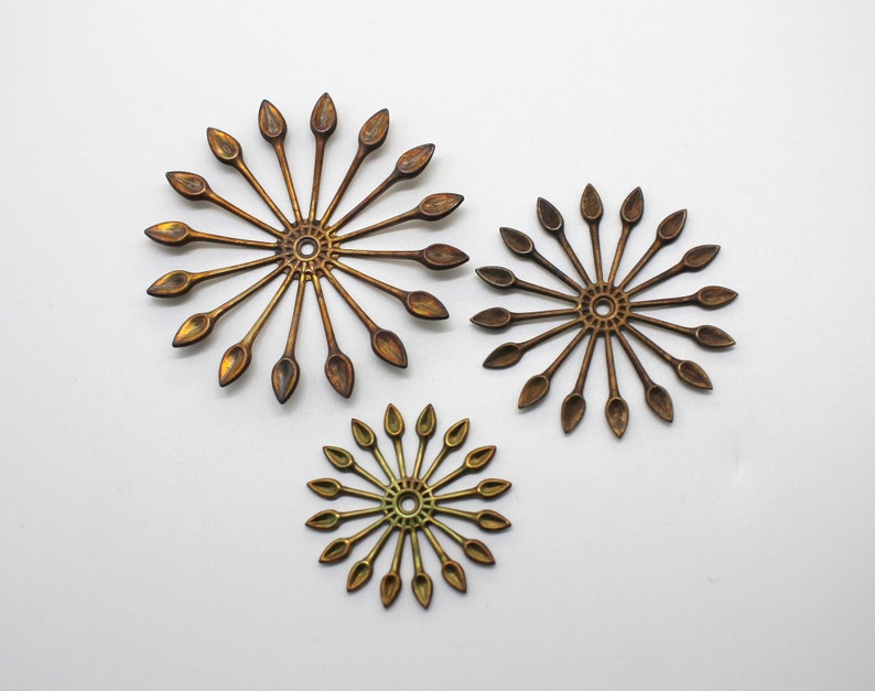 May include: Three gold-toned metal decorative pieces in the shape of a sunburst with pointed rays. The pieces are different sizes and have a slightly aged finish.