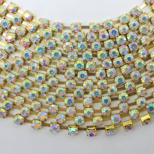 May include: A gold chain with iridescent rhinestones. The chain is made of small, square-shaped rhinestones that are set in a gold metal setting. The chain is about 10 inches long and is perfect for adding a touch of sparkle to any project.