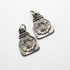 May include: Two silver charm pendants with an ornate design featuring a heart and flames. The pendants are shaped like a small, flat rectangle.