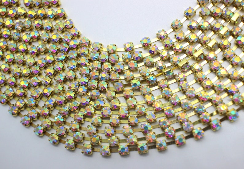 May include: A gold chain with iridescent rhinestones. The chain is made of small, square-shaped rhinestones that are connected by gold metal links.
