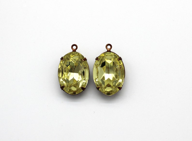 May include: Two oval-shaped, yellow glass pendants with copper-colored metal loops. The pendants have a faceted design.