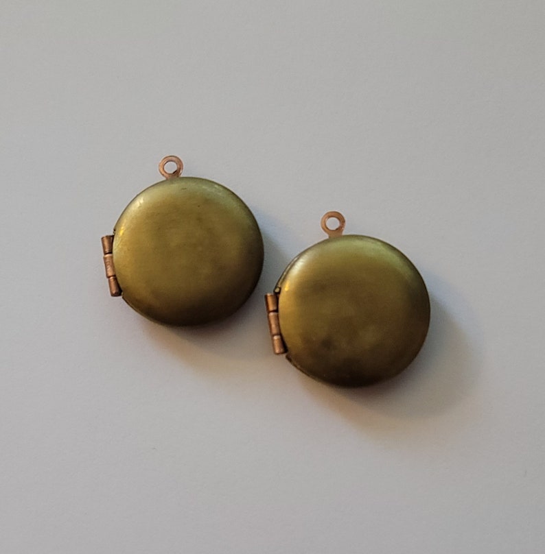 Puede incluir: Dos colgantes de medall&oacute;n redondos de color dorado con una abertura con bisagra. Los medallones tienen un acabado liso y brillante.