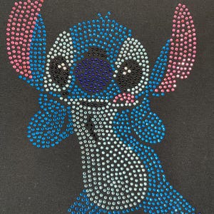 Op de afbeelding: Zwarte afbeelding met een strass-ontwerp van het personage Stitch uit de animatiefilm Lilo & Stitch. Het ontwerp gebruikt blauwe, roze en witte strass-steentjes om de afbeelding van het personage te creëren.