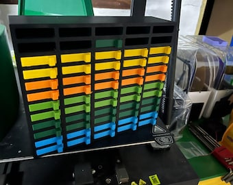 May include: A black, multi-tiered organizer with rows of colorful, rectangular inserts. The inserts are arranged in a gradient of colors, including yellow, orange, green, and blue. The organizer is likely used for storing small items.