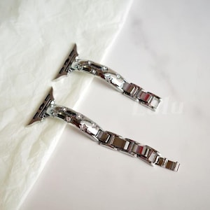 Peut inclure: Deux bracelets de montre en métal argenté avec une finition polie et des cristaux transparents incrustés le long des sections de connexion incurvées. Chaque bracelet comprend une série de maillons rectangulaires fixés à la pièce décorative.