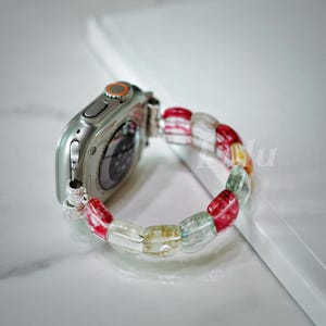 May include: A silver Apple Watch with a colorful beaded band. The band is made of rectangular beads in shades of red, green, and yellow.