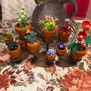 May include: A collection of colorful, miniature succulent plants in orange pots. The plants feature various designs, including green cacti, red flowers, and blue and purple blooms. The plants are arranged on brown stands, creating a decorative display.