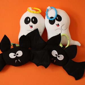 May include: Three Halloween-themed plush toys: two white ghosts with black eyes and a black bat with white eyes. The ghosts have yellow and blue rings around their heads. The bat has a black felt body and wings.
