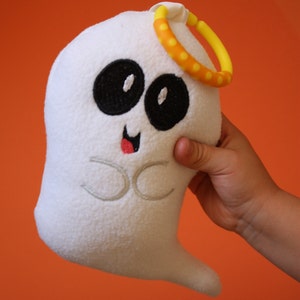 May include: A white plush ghost toy with black eyes and a red mouth. The ghost has a yellow and orange ring around its head.