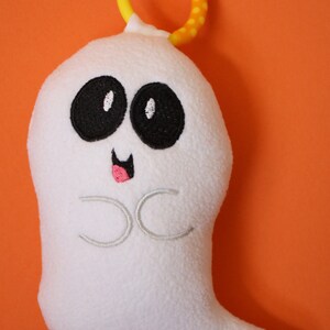 May include: White plush ghost toy with embroidered eyes, a pink mouth, and the letters "CC" on the front. The ghost has a yellow and orange teething ring attached to the top.