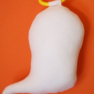 May include: White plush ghost with a yellow and orange halo. The ghost has a long tail and is sitting on an orange background.