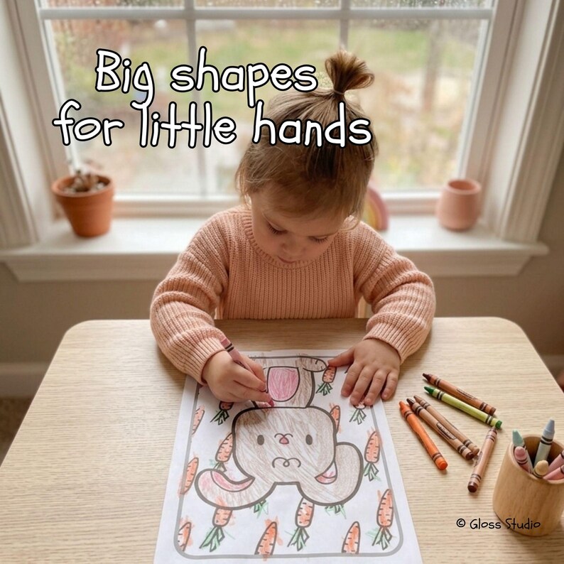May include: A child coloring a bunny and carrot drawing with crayons. The image includes the text "Big shapes for little hands". A wooden cup holds several crayons. The child is wearing a peach-colored sweater.