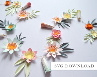 Può includere: Una ghirlanda di fiori di carta con fiori e foglie di colore rosa pastello, giallo, arancione e verde. La ghirlanda è infilata su uno spago bianco e ha piccoli pon pon che pendono tra i fiori. Il testo "SVG DOWNLOAD" è in basso nell'immagine.