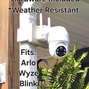 May include: White outdoor security camera with two antennas, mounted on a white bracket. The camera is weather resistant and includes hardware. Text on the image says "Easily repositioned", "Fits: Arlo, Wyze, Blink, Eufy and more!"