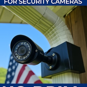 May include: A black clamp-on gutter mount for security cameras. The mount is attached to a gutter and holds a black security camera. Text on the image reads "CLAMP-ON GUTTER MOUNT FOR SECURITY CAMERAS" and "NO-DRILL NEEDED". An American flag is in the background.