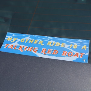 May include: A rectangular bumper sticker featuring a light blue water pattern background with the text MY OTHER RIDE IS A TALKING RED BOAT in yellow and red lettering, accompanied by a small white graphic of a lobster in the bottom right corner.