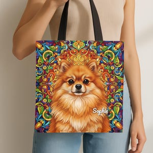 May include: A tote bag with a detailed illustration of a Pomeranian dog with fluffy orange fur. The dog is centered against a vibrant, colourful stained-glass style background. The name "Sophie" is written on the bag. The bag has black handles.