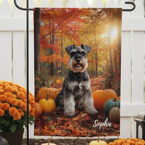 Puede incluir: Una bandera de jardín con un perro Schnauzer sentado entre calabazas y hojas de otoño en un entorno forestal. La bandera tiene el nombre "Sophie" impreso. La escena está rodeada de crisantemos naranjas, calabazas y faroles.