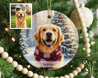 May include: A round ceramic Christmas ornament featuring a golden retriever wearing a dark red scarf with white snowflake patterns. The name Sophie is printed in black script at the bottom. A small inset photo shows the same dog in a yard.