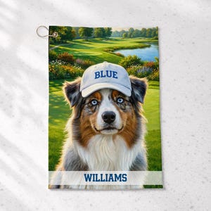 May include: A rectangular golf towel featuring a printed image of an Australian Shepherd dog wearing a light gray baseball cap with the word BLUE in blue text. The dog is positioned against a golf course background with the name WILLIAMS in blue.
