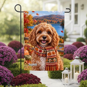 May include: A rectangular garden flag featuring a portrait of a golden-brown curly-haired dog wearing a knit scarf with pumpkin, leaf, and mug patterns. The background shows a lake and autumn trees. The name Sophie is printed in white.