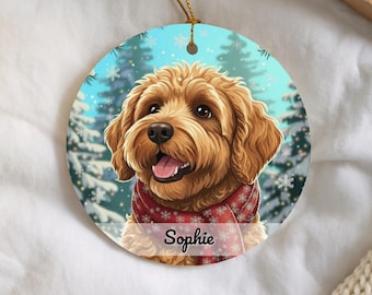 May include: A round ceramic ornament featuring a fluffy golden-brown dog wearing a red scarf with white snowflake patterns. The background shows a winter forest scene with falling snowflakes. The name Sophie is printed in black script at the bottom.