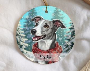 May include: A round ceramic ornament featuring a grey and white dog wearing a red scarf with a white snowflake pattern. The background shows a snowy forest with falling snowflakes. The name Sophie is printed in black script on the dog's scarf.