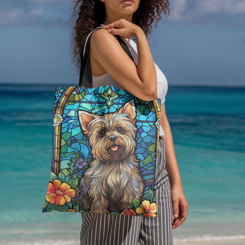 a woman standing on a beach holding a bag with a picture of a yorkshire terrier yorkie dog on