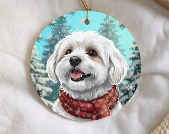 Puede incluir: Un adorno redondo de cerámica con un perro blanco de pelaje esponjoso que lleva una bufanda roja con un patrón de copos de nieve blancos. El fondo muestra una escena invernal con pinos nevados y copos cayendo bajo un cielo azul claro.