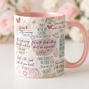 May include: A white ceramic mug with a pink handle and interior. The mug is decorated with inspirational quotes, butterflies, flowers, and a rainbow design. The text includes Bible verses and phrases.