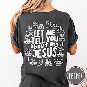 May include: A charcoal gray t-shirt featuring white screen-printed text on the back that reads, Let me tell you about my Jesus, surrounded by various religious icons and scripture references including a dove, a bible, a rainbow, and a crown.