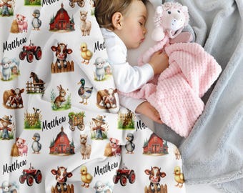 May include: A white baby blanket with a farm animal pattern, including a red tractor, barn, and various animals. The name "Matthew" is printed on the blanket in black script. A sleeping child is wrapped in the blanket, holding a pink plush toy.