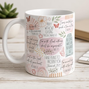 May include: White ceramic mug with inspirational quotes and floral illustrations in pink, peach, and green. The mug has a curved handle and is designed for hot drinks. The design includes butterflies, flowers, and rainbow elements.