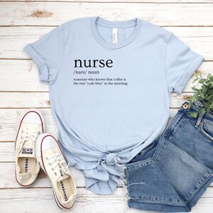 May include: Light blue t-shirt with the word "nurse" defined as "someone who knows that coffee is the real 'code blue' in the morning."