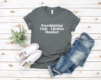 May include: A dark gray t-shirt with the text "Overthinking Club - Lifetime Member" in white lettering.