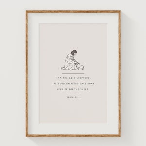 May include: A framed print with a minimalist line drawing of a figure and a sheep. The artwork is in a wooden frame with a white mount. Text reads "I AM THE GOOD SHEPHERD...HIS LIFE FOR THE SHEEP." John 10:11.