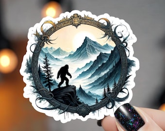 May include: A circular sticker featuring a dark, ornate frame surrounding a landscape illustration. The scene depicts a silhouette of a large, bipedal creature standing on a rocky cliff overlooking a range of blue, snow-capped mountains and pine trees.