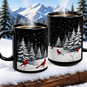Puede incluir: Dos tazas de cerámica negras con una escena invernal que presenta cardenales rojos, pinos cubiertos de nieve y un paisaje nevado. Las tazas tienen un fondo negro con copos de nieve blancos y vapor que se eleva del café.