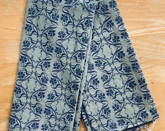 May include: Two folded, light green kitchen towels with a repeating dark blue floral pattern. The towels are made of a textured fabric and have small tags attached. The floral design features stylized flowers and vines.