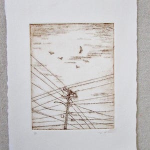 May include: A sepia-toned etching print of a utility pole with crisscrossing power lines and birds in flight against a cloudy sky. The artwork is on textured, deckle-edged paper, creating a rustic aesthetic. The print is mounted on a white mat.